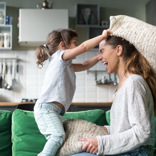 Eine Mutter und ihre Tochter veranstalten eine Kissenschlacht auf dem Sofa. 
