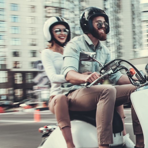 Eine Frau und ein Mann fahren auf einer Vespa durch die Stadt.