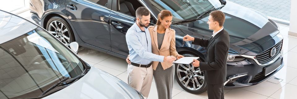 Ein junges Paar kauft ein Auto und bekommt den Schlüssel vom Verkäufer übergeben.